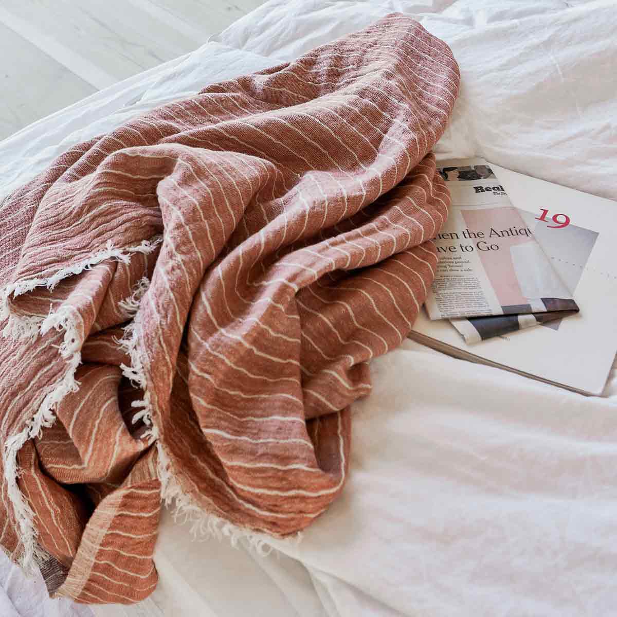 kissenhuelle_canva_house_doctor_6 Rote Decke mit Streifen und Fransen - im Bett neben einer Zeitung