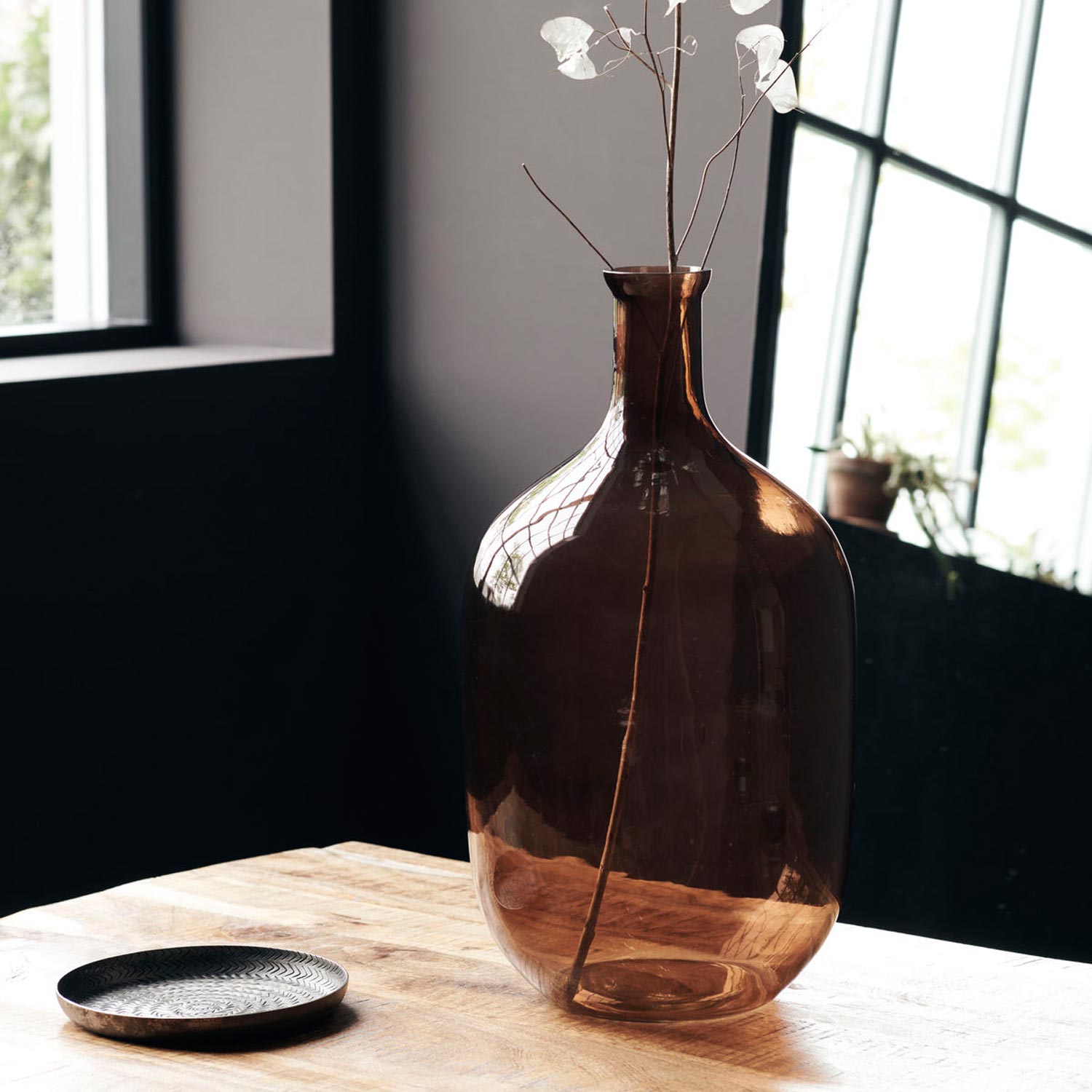 Große Bodenvase aus braunem Glas mit Deko auf Tisch